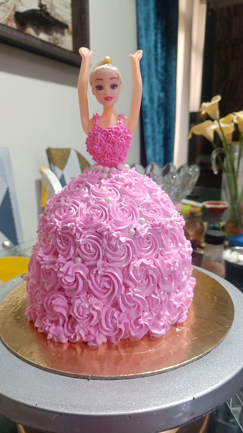 Doll cake with a plastic Barbie figure rising from a dome of pink buttercream piped as a rosette ball gown skirt, arms raised overhead, pearl beading at the waistline